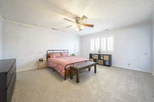 Bedroom featuring light carpet, a textured ceiling, ornamental molding, and ceiling fan