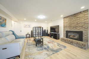 Living room with recessed lighting, a brick fireplace, and light wood-style floors