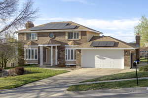 View of front facade featuring roof mounted solar panels, brick siding, an attached garage, and a chimney