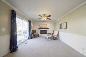 Sitting room featuring a fireplace with raised hearth, carpet, ornamental molding, and ceiling fan
