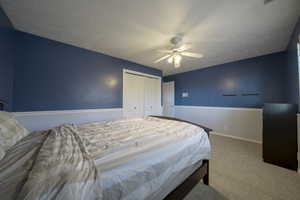 Bedroom with light carpet, a textured ceiling, wainscoting, a closet, and a ceiling fan