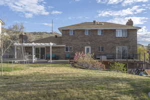 Rear view of property with a deck, a trampoline, brick siding, and a lawn