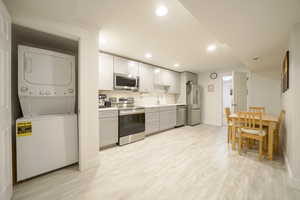 Kitchen with stainless steel appliances, light countertops, light wood-type flooring, recessed lighting, and stacked washer and clothes dryer