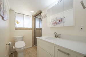 Full bathroom with vanity, a shower stall, light tile patterned floors, a textured ceiling, and recessed lighting