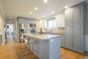 Kitchen with light stone counters, stainless steel appliances, light wood finished floors, a kitchen breakfast bar, and tasteful backsplash