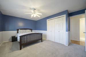 Bedroom featuring carpet flooring, a closet, a textured ceiling, a ceiling fan, and a wainscoted wall