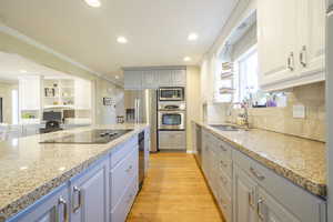 Kitchen with light wood finished floors, stainless steel appliances, crown molding, decorative backsplash, and light stone countertops