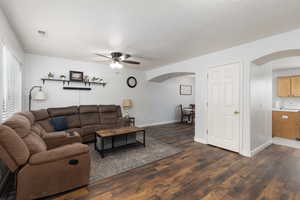 Living room with dark wood-style floors, a ceiling fan, a textured ceiling, and arched walkways