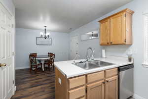 Kitchen with stainless steel dishwasher, a peninsula, light countertops, hanging lights, and a textured ceiling