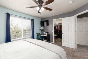 Carpeted bedroom with a walk in closet, a textured ceiling, ceiling fan, and a desk