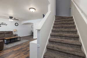 Stairway with a textured ceiling, ceiling fan, wood finished floors, and arched walkways