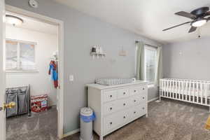 Bedroom with dark carpet, a nursery area, ceiling fan, and a walk in closet