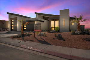 Modern home featuring an attached garage, driveway, a chimney, and stucco siding