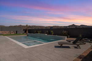 Pool at dusk featuring a fenced backyard, a patio, and a pool with connected hot tub