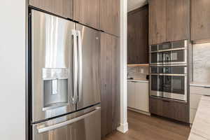 Kitchen featuring stainless steel appliances, modern cabinets, decorative backsplash, and dark wood-style flooring