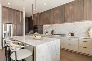 Kitchen featuring modern cabinets, a kitchen breakfast bar, stainless steel appliances, light stone countertops, and light wood-type flooring