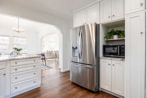 Kitchen featuring stainless steel fridge, light stone countertops, white cabinets, arched walkways, and dark wood-style flooring