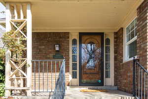 Doorway to property featuring brick siding and covered porch