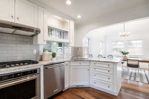Kitchen with stainless steel appliances, a peninsula, light stone counters, white cabinetry, and dark wood-type flooring