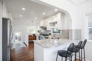 Kitchen featuring light stone counters, stainless steel appliances, white cabinets, a peninsula, and a breakfast bar area