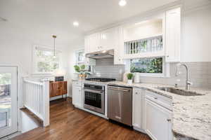 Kitchen with white cabinetry, stainless steel appliances, light stone countertops, dark wood finished floors, and pendant lighting