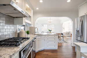 Kitchen with light stone counters, white cabinetry, stainless steel appliances, suspended lighting, and a peninsula