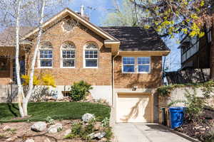 View of front of house with brick siding, a garage, a front lawn, concrete driveway, and a chimney