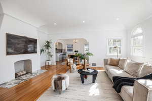 Living room featuring light wood finished floors, arched walkways, suspended lighting, and a fireplace with flush hearth