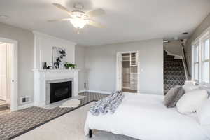 Carpeted bedroom featuring a spacious closet, a ceiling fan, and a fireplace with flush hearth