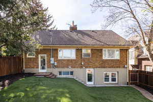 Rear view of house with a fenced backyard, brick siding, a chimney, a gate, and roof with shingles