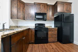 Kitchen with black appliances, dark wood finish cabinetry, light stone counters, and dark wood-style floors