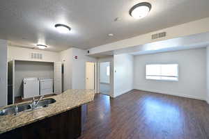 Kitchen with dark wood-type flooring, a textured ceiling, washing machine and clothes dryer, light stone countertops, and dark wood finish cabinetry