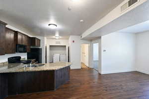 Kitchen featuring dark wood finish cabinets, dark wood finished floors, a peninsula, black appliances, and a textured ceiling