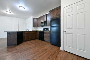 Kitchen featuring dark wood finish cabinets, black appliances, dark wood-type flooring, a textured ceiling, and a peninsula