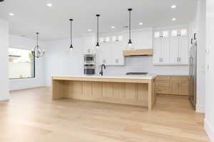 Two tone kitchen featuring light wood-type flooring, a kitchen island with sink, decorative backsplash, two tone color scheme, and stainless steel appliances