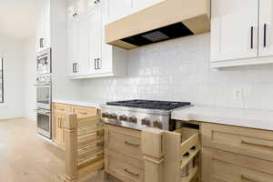 Kitchen featuring stainless steel appliances, light wood finished floors, decorative backsplash, and two tone cabinets