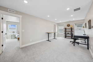 Home office with light colored carpet and recessed lighting