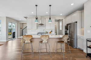 Kitchen featuring a kitchen island with sink, stainless steel appliances, dark wood-type flooring, hanging light fixtures, and white cabinetry