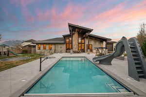 Rear view of property featuring a playground, a patio, and stone siding