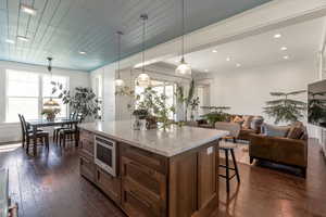 Kitchen with light stone counters, pendant lighting, open floor plan, dark wood-style flooring, and a kitchen island