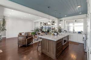 Two tone kitchen featuring open floor plan, two tone cabinets, a breakfast bar area, dark wood finished floors, and light stone counters