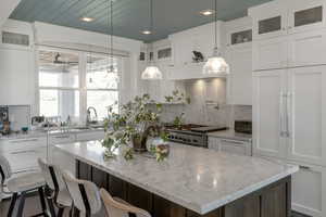 Dual tone kitchen with glass insert cabinets, light stone counters, tasteful backsplash, and two tone cabinets