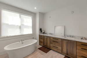 Bathroom with double vanity, a freestanding tub, recessed lighting, and light marble finish flooring
