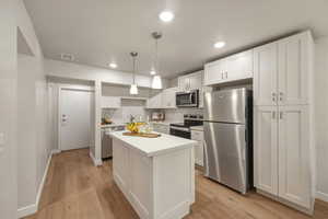 Kitchen with stainless steel appliances, white cabinets, light countertops, light wood-style flooring, and hanging light fixtures