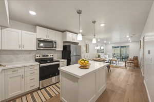 Kitchen with stainless steel appliances, backsplash, white cabinets, and light countertops