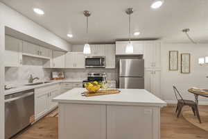 Kitchen with white cabinetry, stainless steel appliances, light wood finished floors, and decorative light fixtures