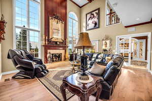 Living room featuring a fireplace, light wood-style floors, a high ceiling, french doors, and ornamental molding