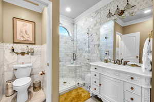 Bathroom featuring a stall shower, vanity, crown molding, and tile walls
