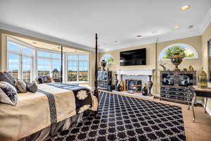 Bedroom featuring ornamental molding, a lit fireplace, and light colored carpet