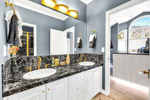 Bathroom with tasteful backsplash, double vanity, crown molding, light wood-style flooring, and lofted ceiling